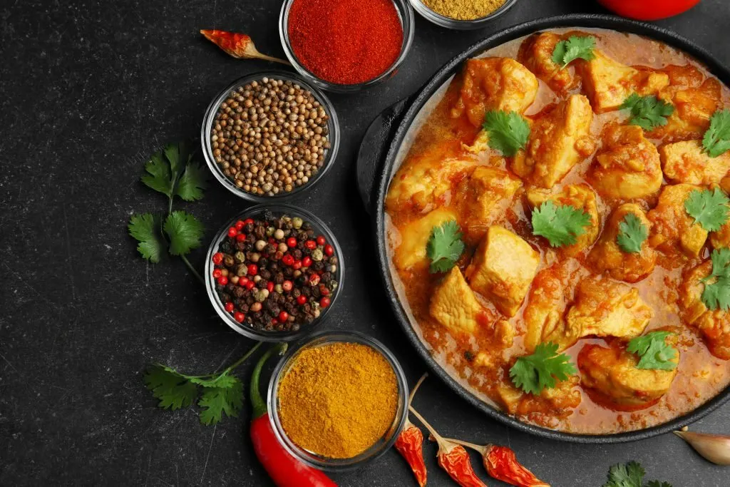 A chicken curry surrounded by bowls of freshly ground spices